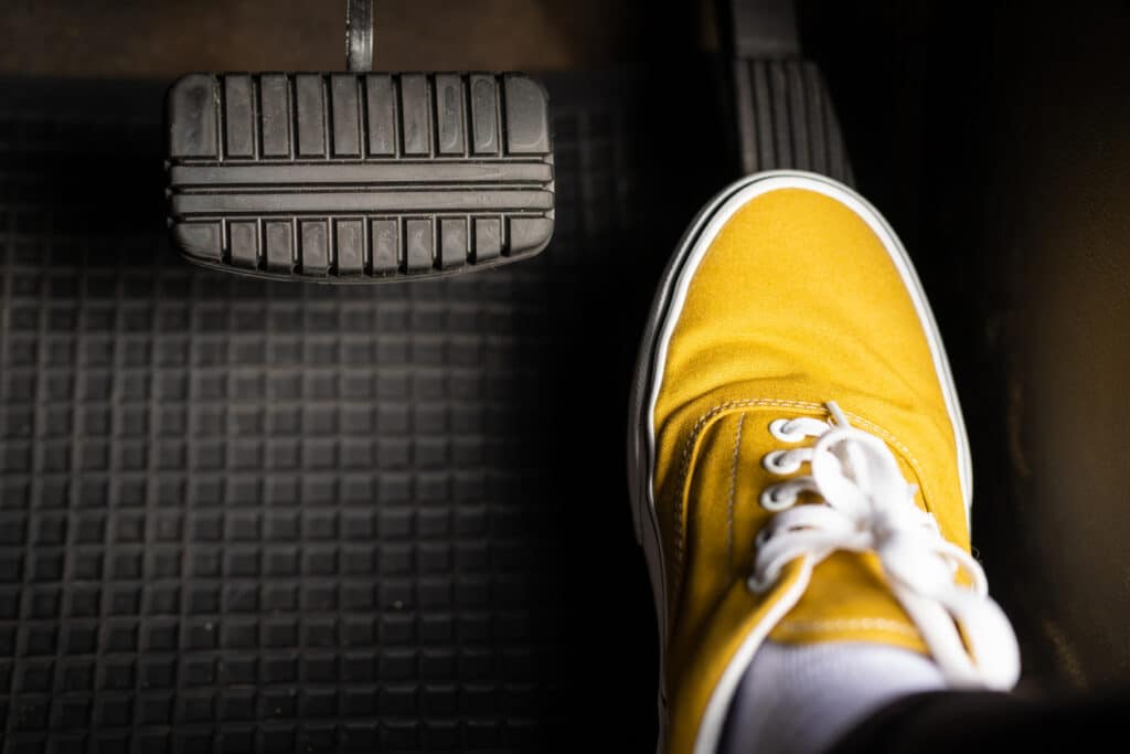 A man in yellow sneakers is stepping on the accelerator of a car.