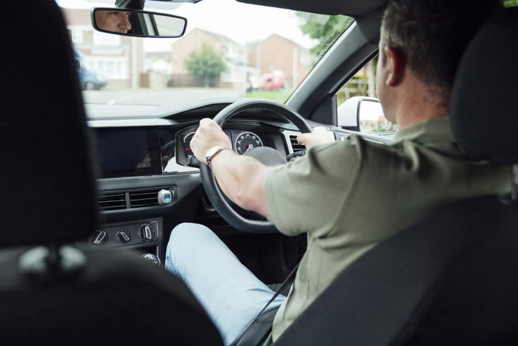 A shot of a 40yr old Caucasian male's hands on the driver's steering wheel.