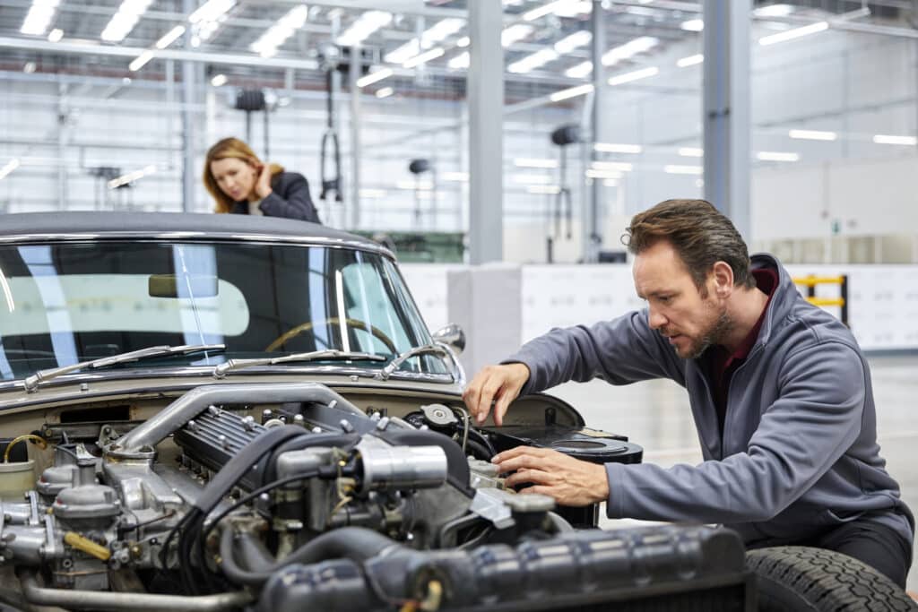 Male mechanic fixing car whilst female customer looks on from behind